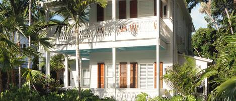 A two-story house with a balcony, surrounded by tropical vegetation.