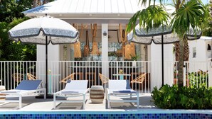 A poolside area with lounge chairs, umbrellas, and a covered seating area with hanging lights. - Winslow's Bungalows - Key West Historic Inns (Key West)