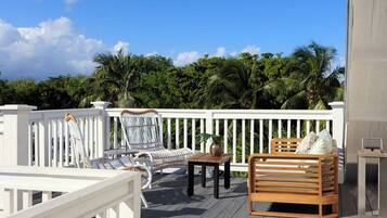 Une terrasse avec des balustrades blanches, un banc en bois et deux chaises en osier.