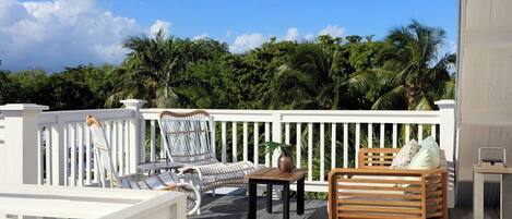 A deck with white railings, a wooden bench, and two wicker chairs.