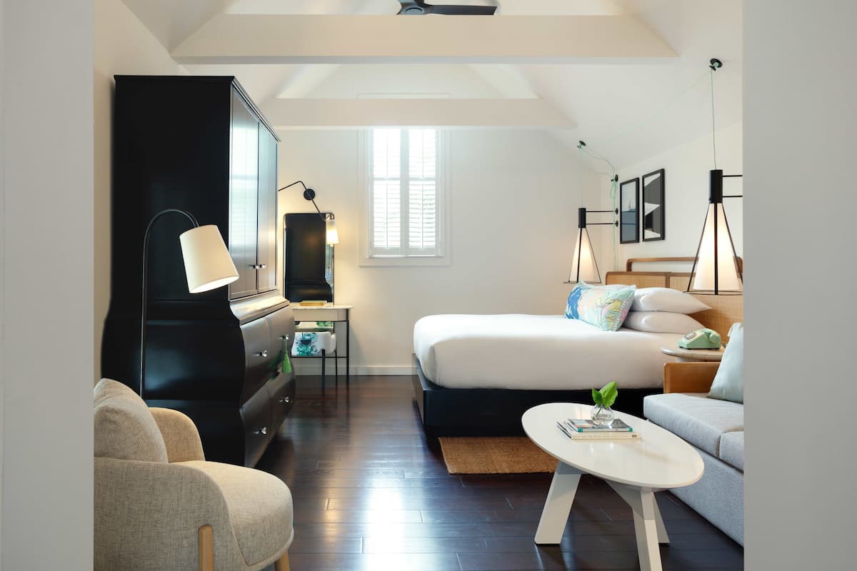 A modern hotel room with a bed, sofa, and a desk with a lamp.