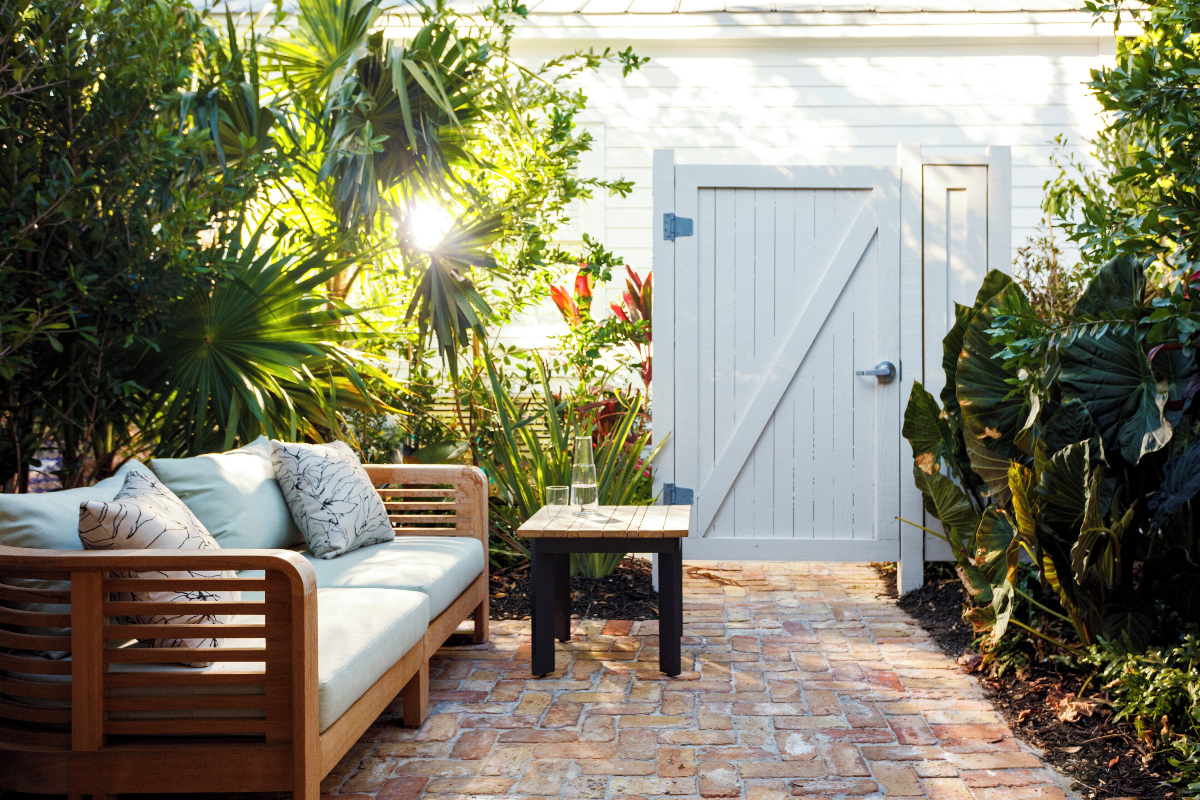 A wooden bench, a small table, and a white door in a garden with plants and a brick pathway.