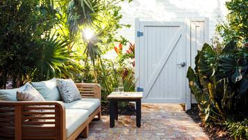 A wooden bench, a small table, and a white door in a garden with plants and a brick pathway.