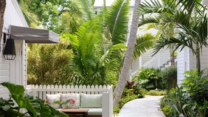 A white picket fence, a wooden bench with cushions, and a concrete pathway surrounded by lush greenery. - Winslow's Bungalows - Key West Historic Inns (Key West)