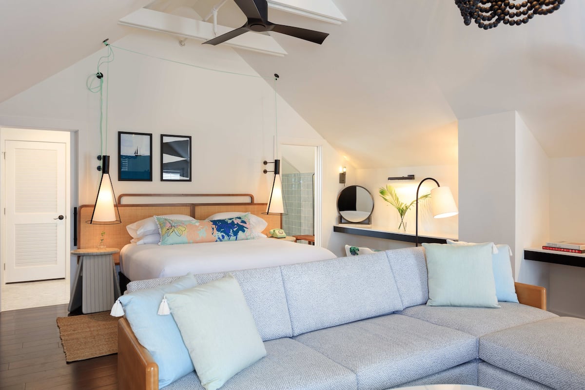 A modern bedroom with a bed, a sofa, a ceiling fan, and a wall-mounted mirror.