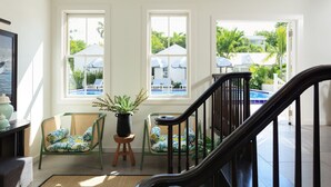 A bright room with a staircase, two windows overlooking a pool area, and two wicker chairs with cushions. - Winslow's Bungalows - Key West Historic Inns (Key West)