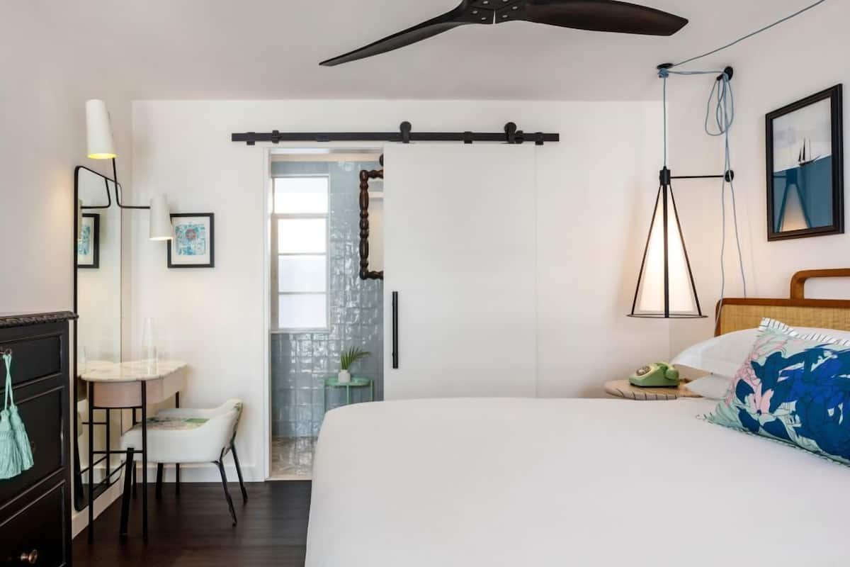 A modern bedroom with a bed, bedside table, lamp, and a ceiling fan.