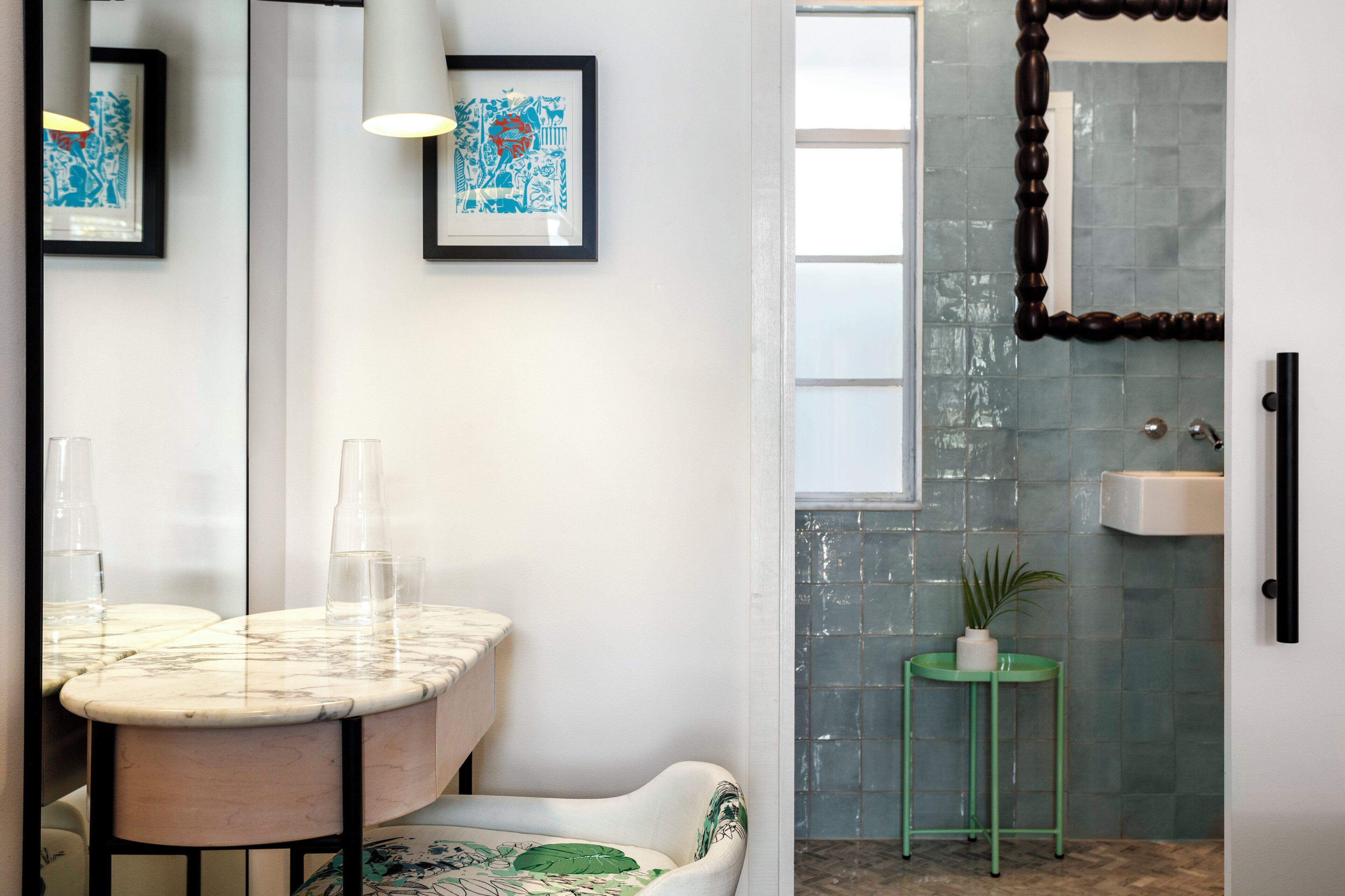 A bathroom with a marble vanity, a green stool, a potted plant, a mirror, and a tiled shower area.