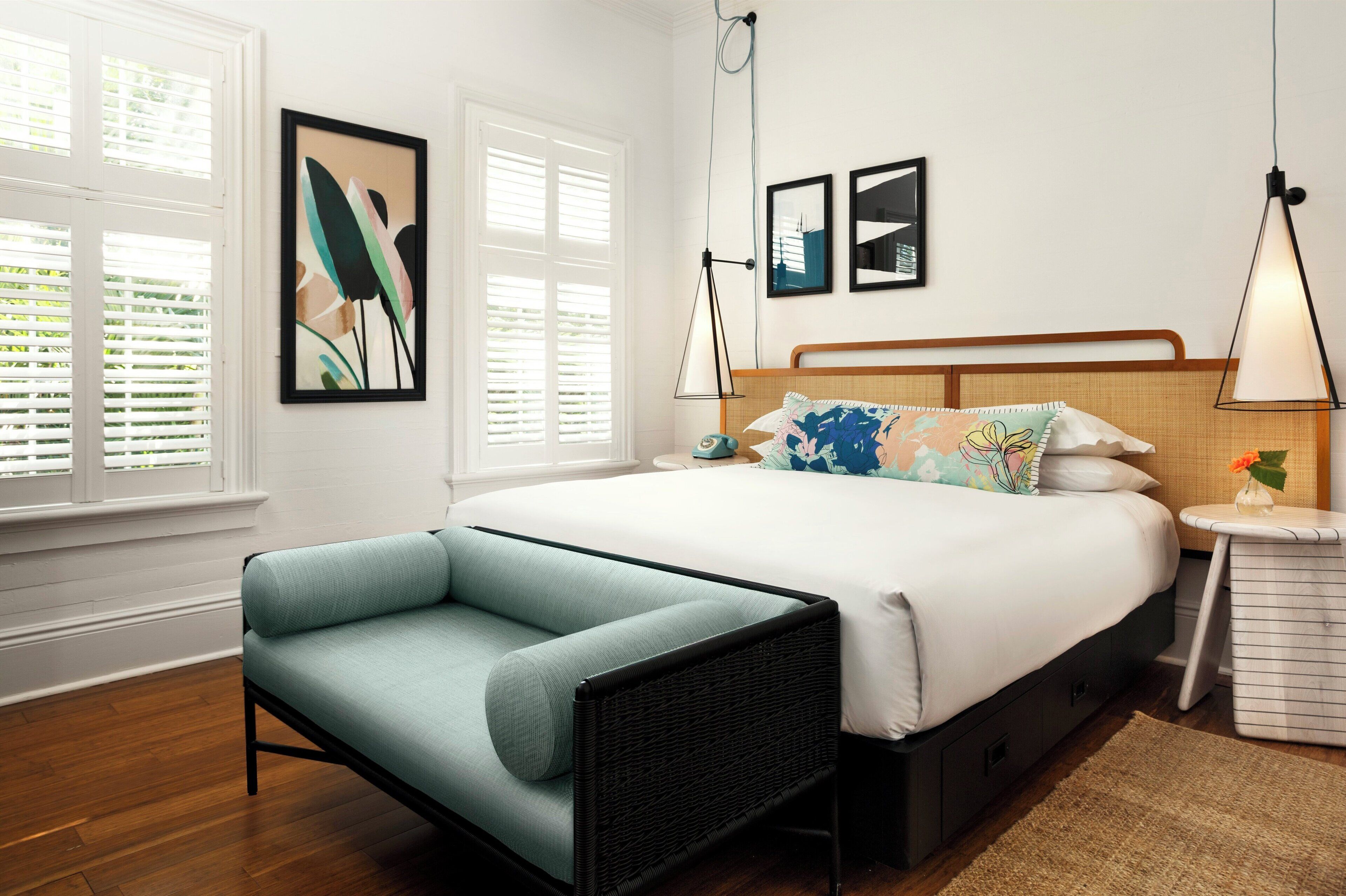 A bedroom with a bed, a chair, a nightstand, and a wall-mounted lamp.