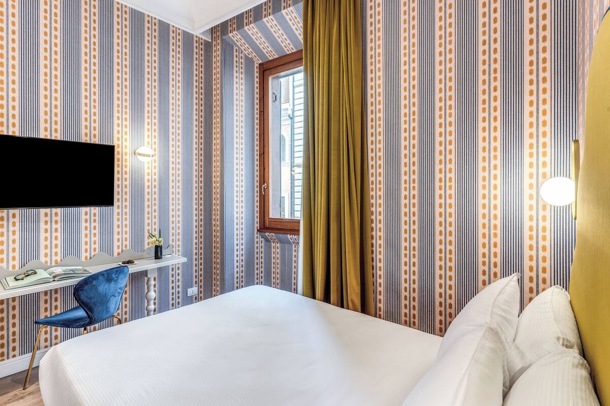 Ett hotellrum med en säng, ett skrivbord med en stol, en tv och randiga tapeter.