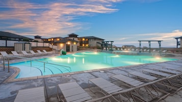 Una piscina con sillones de descanso, un área techada y edificios al fondo.
