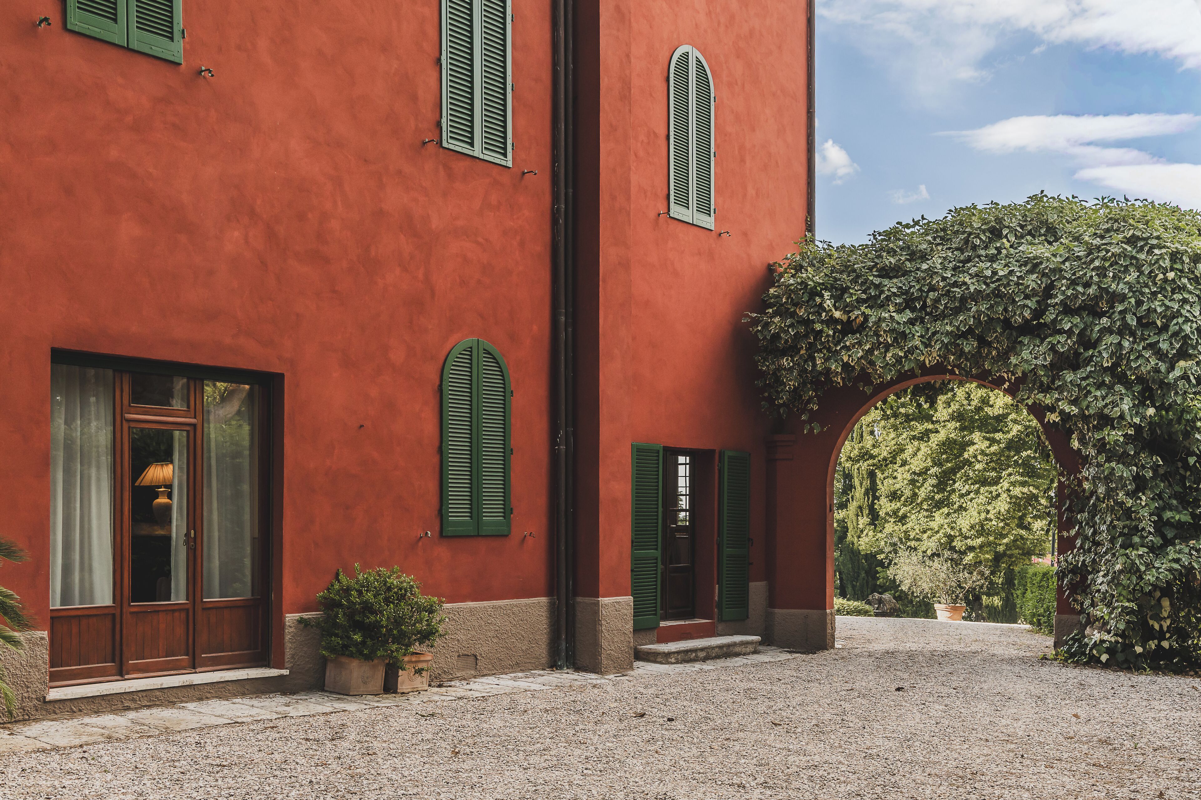 Un edificio con fachada roja, contraventanas verdes y un patio de grava.