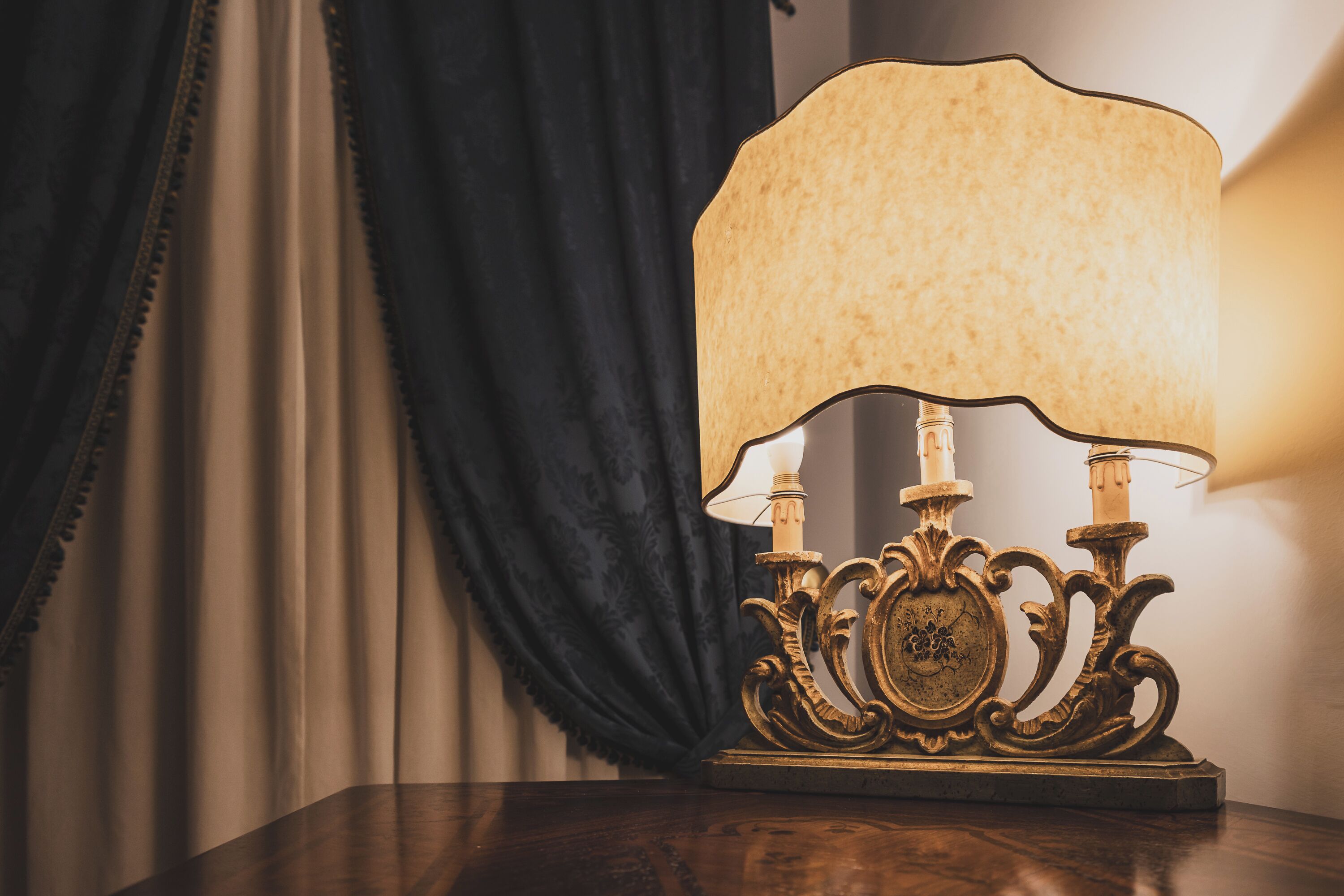 A table lamp with a decorative base and a lighted lampshade on a wooden surface.