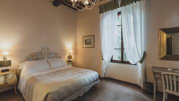 Un dormitorio con cama con dosel, una araña, un escritorio con silla y una ventana con cortinas.