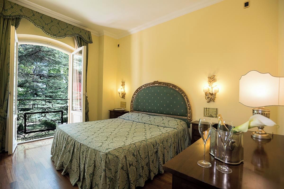 Une chambre à coucher comprenant un lit, deux lampes de chevet, une table de chevet, une fenêtre avec des rideaux et une vue sur la verdure à l’extérieur.