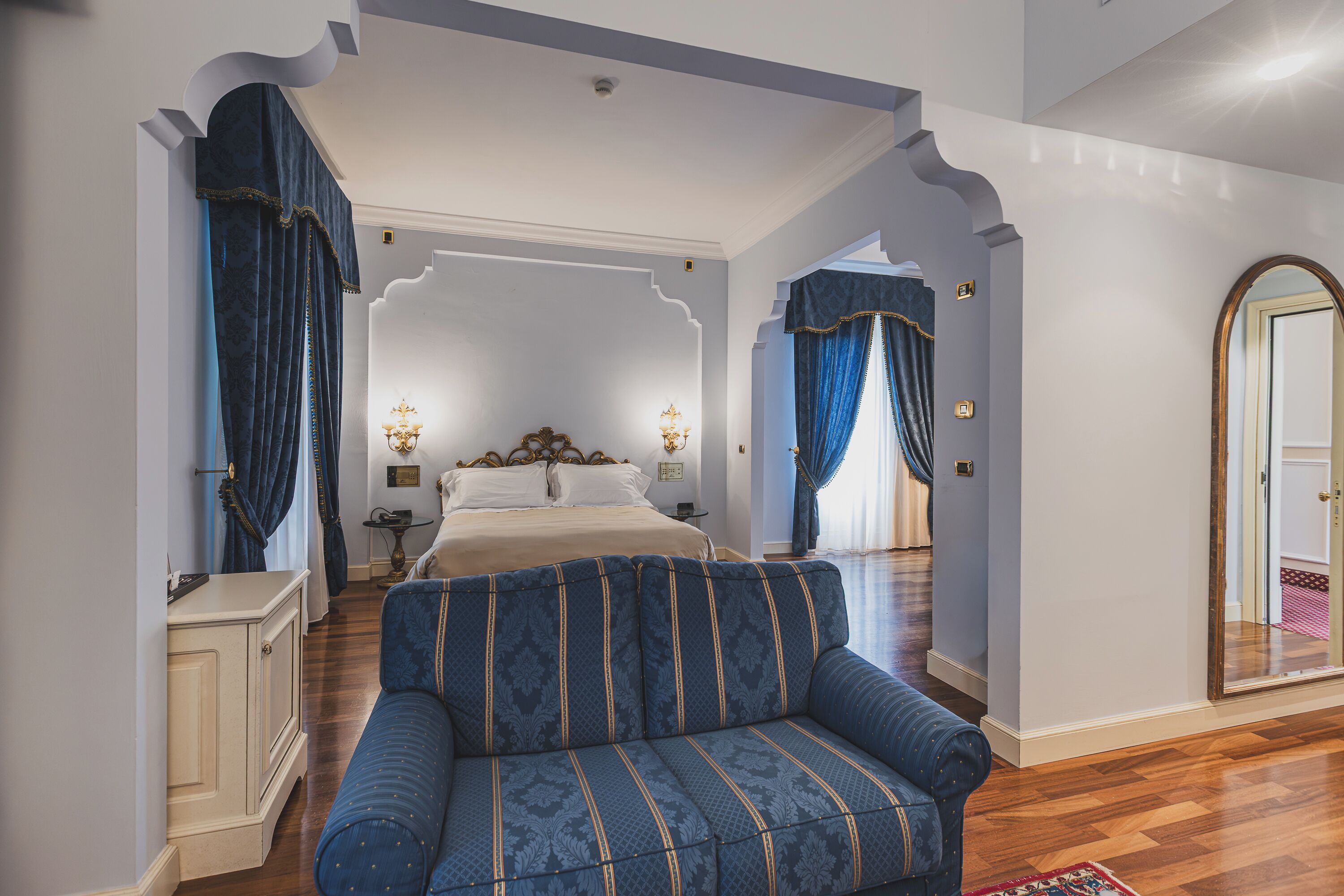A bedroom with a large bed, a sofa, a wardrobe, and a mirror.