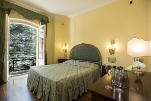 Relax in a classic room with a large bed, bedside lamps, and a serene view of lush greenery.