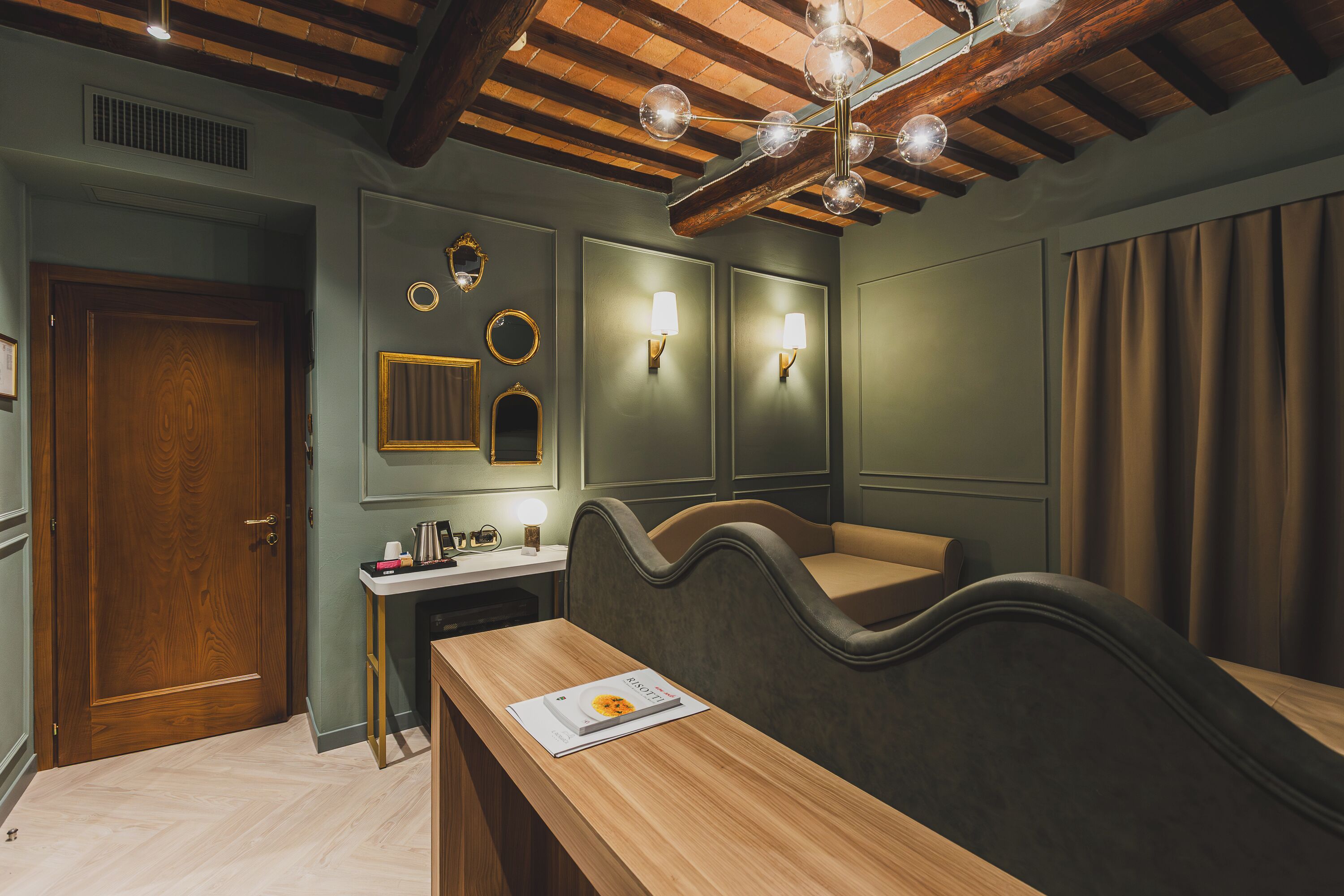 Una stanza con soffitto in legno, una scrivania con un libro, una panca e luci a parete.