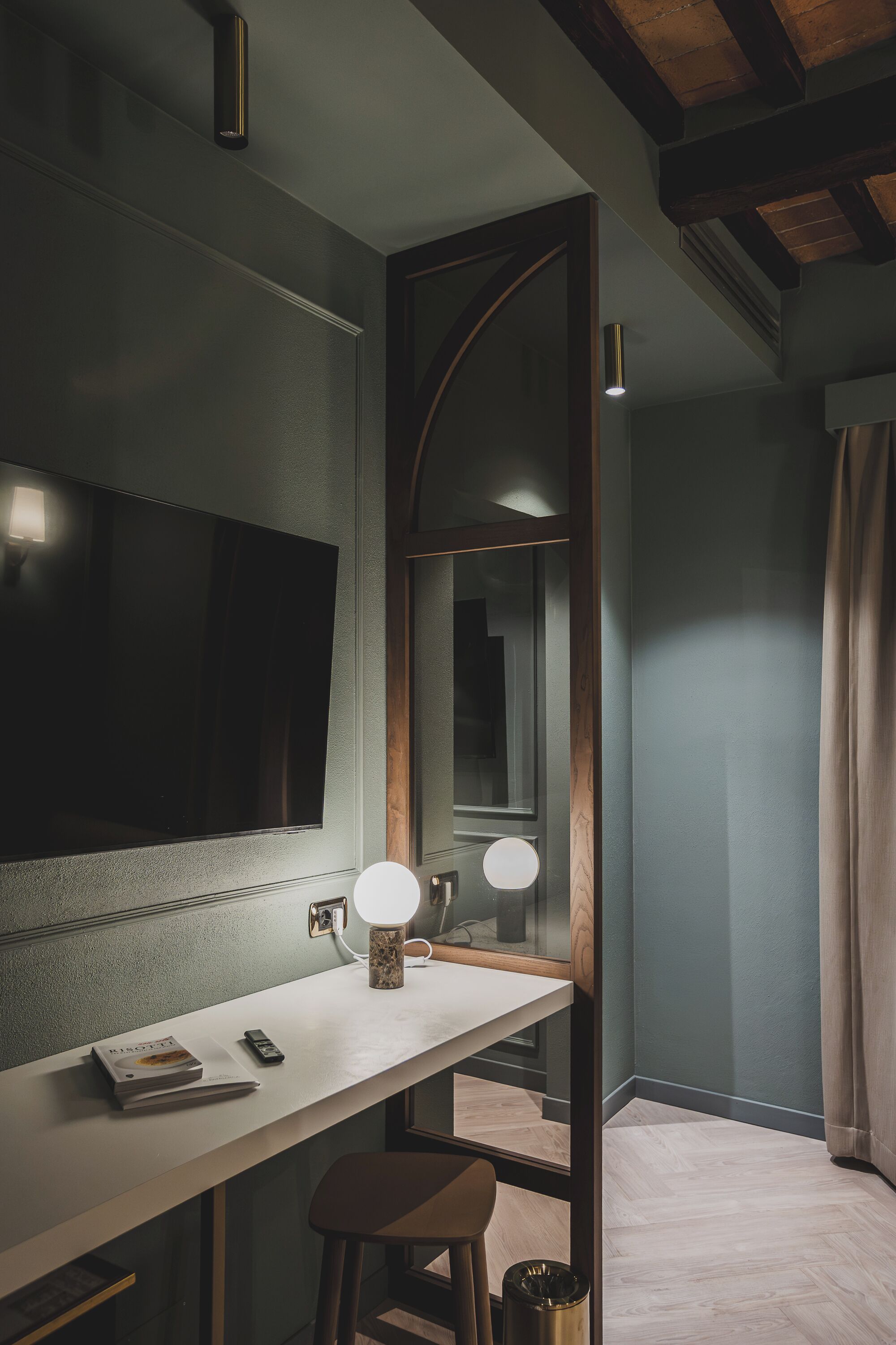 Ein Zimmer mit einem großen Flachbildfernseher an der Wand, einem Schreibtisch mit Lampe, einem Spiegel und einem Hocker.