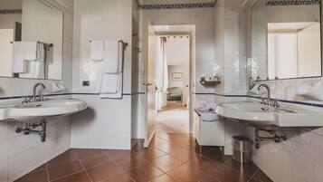 Une salle de bain avec deux lavabos, des murs recouverts de carreaux blancs et un sol carrelé de couleur marron.
