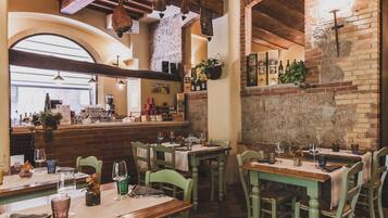 Interior de restaurante con paredes de ladrillo, vigas de madera y mesas preparadas para comer.