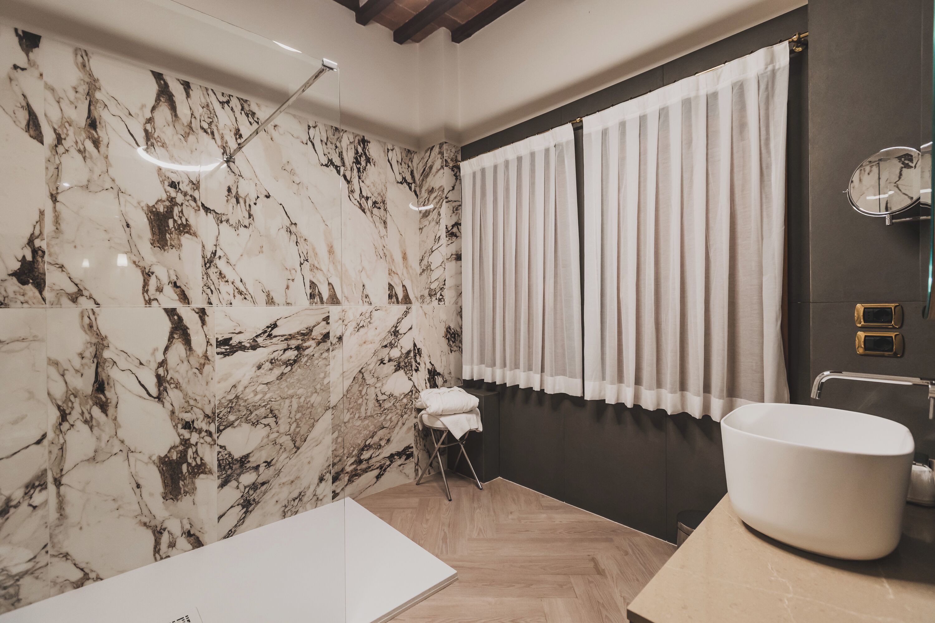 Un baño con pared de mármol, un lavamanos grande y suelo de madera.
