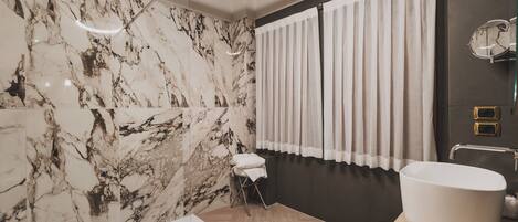 Un baño con pared de mármol, un lavamanos grande y suelo de madera.