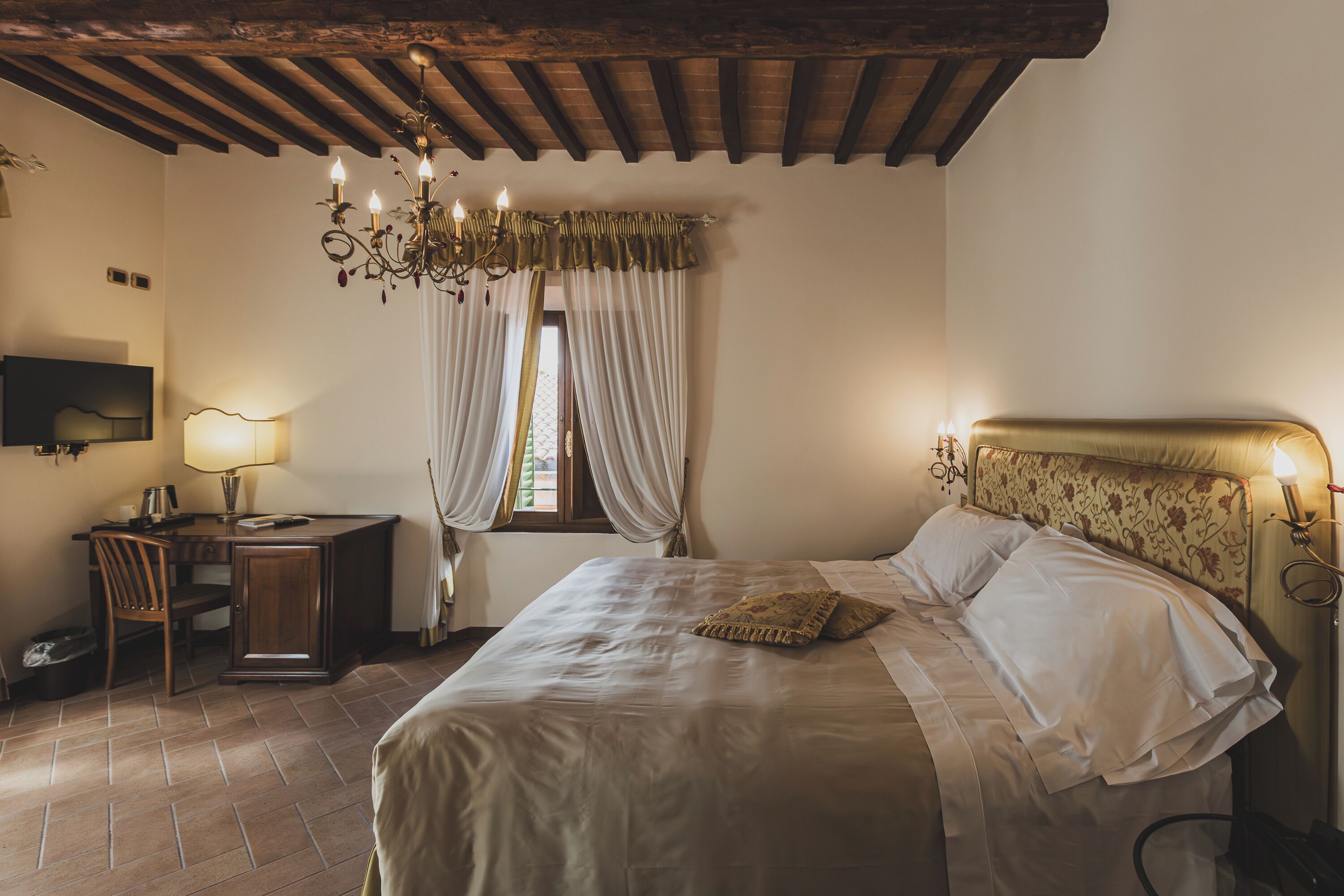 Ein Schlafzimmer mit einem Bett, einem Schreibtisch, einem Sessel, einem Fernseher und einer Chandelüster.