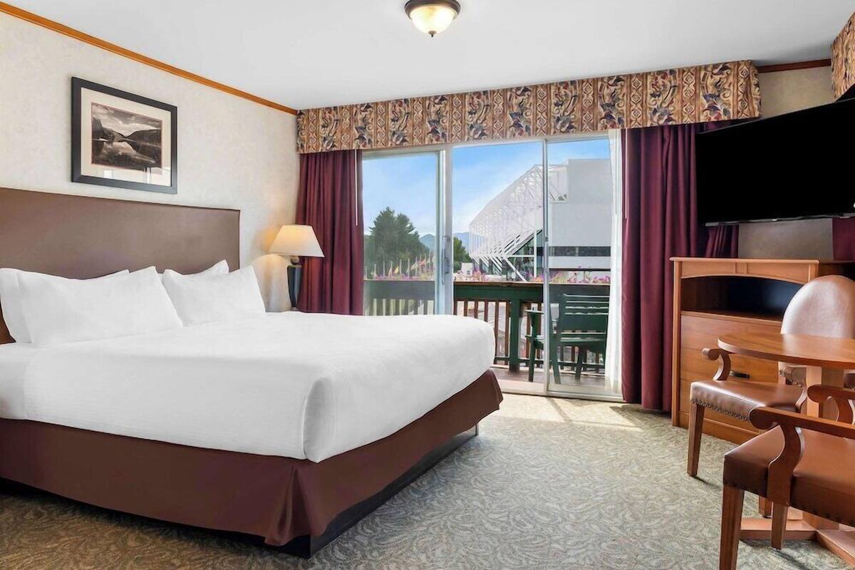 A hotel room with a large bed, a desk, a chair, a TV, and a balcony with a view.