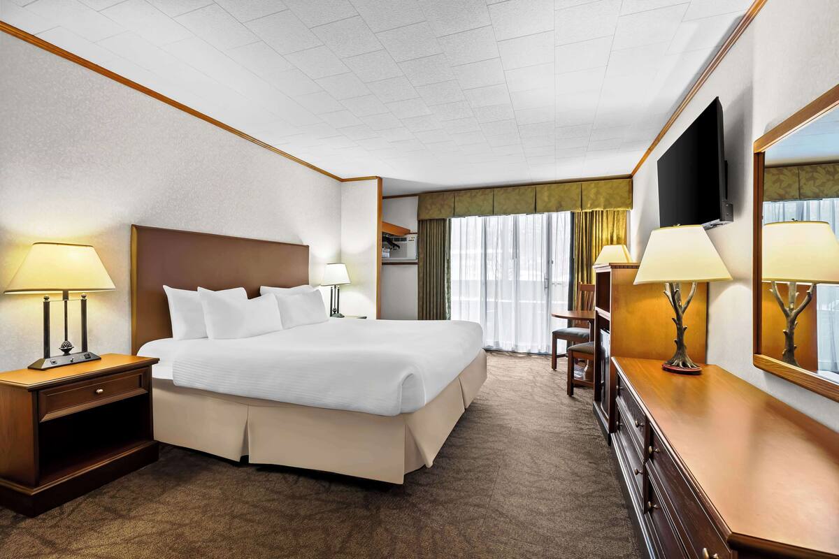 A hotel room with a large bed, two bedside tables with lamps, a flat-screen TV mounted on the wall, and a large mirror.