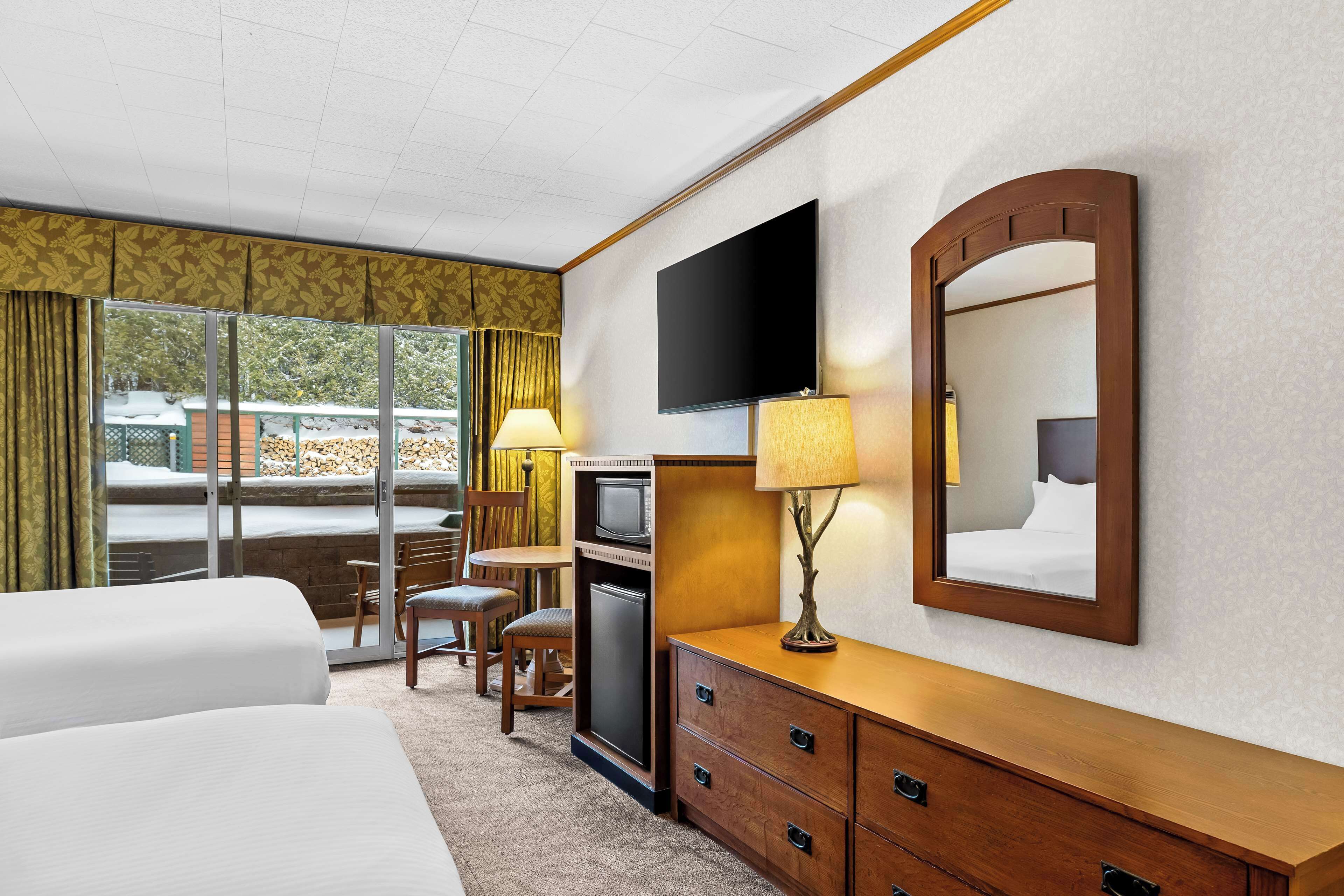 A hotel room with a bed, a desk with a computer, a TV, a mirror, and a view of the outdoors.