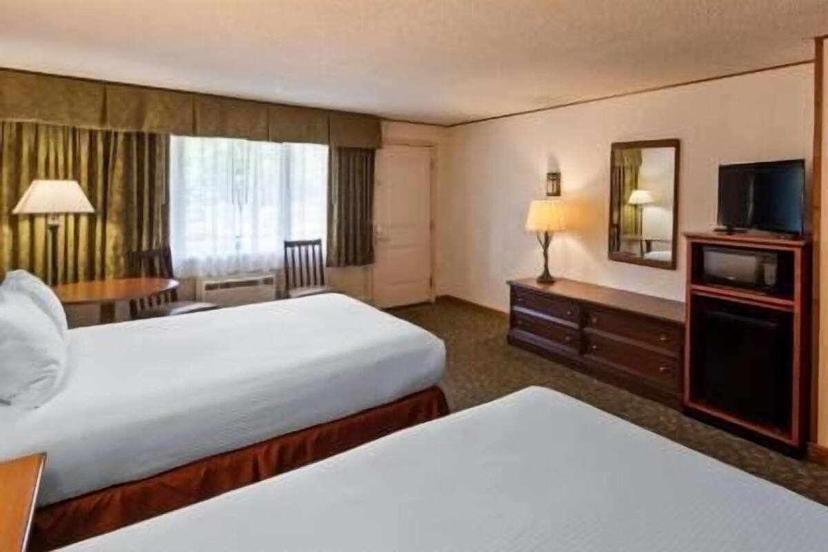 A hotel room with two beds, a desk, a chair, a TV, and a wardrobe.