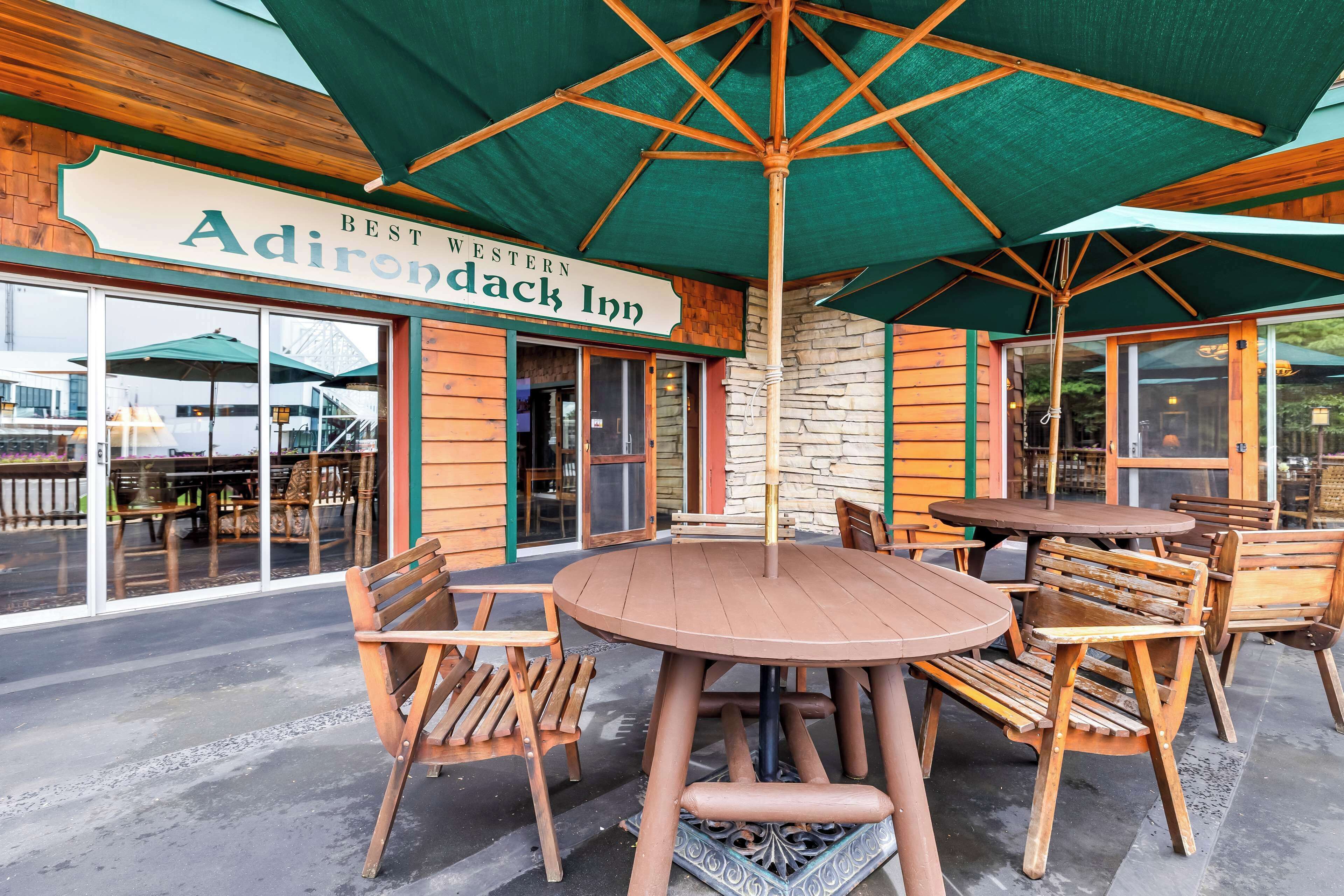 An outdoor seating area with wooden tables and chairs, a large umbrella, and a sign for Adirondack Inn.