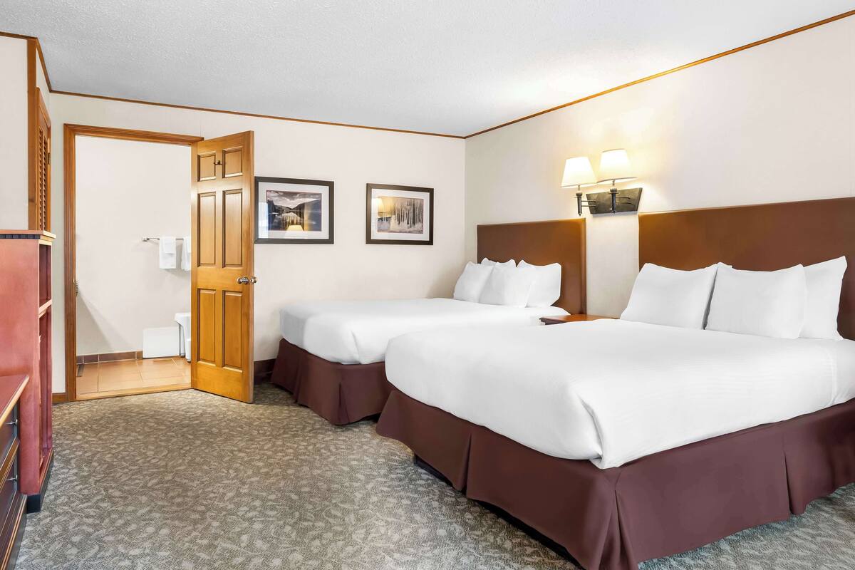 A hotel room with two beds, a wooden door, and two framed pictures on the wall.