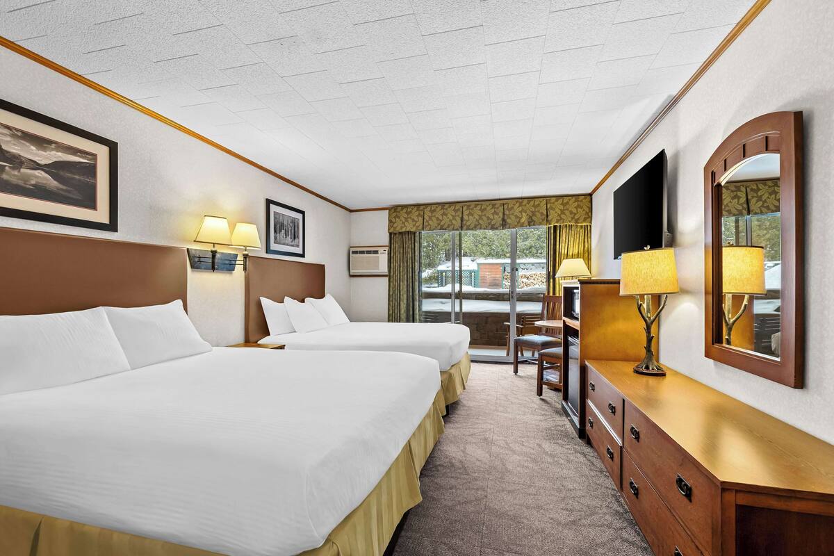 A hotel room with two beds, a wooden dresser, a TV, and a window with curtains.
