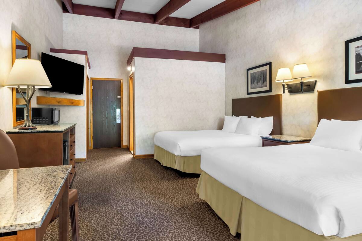A hotel room with two beds, a desk with a lamp, a TV, and a microwave.