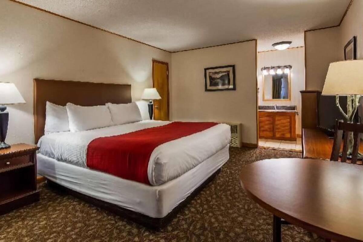 A hotel room with a bed, two bedside tables, a desk, a chair, and a window with curtains.