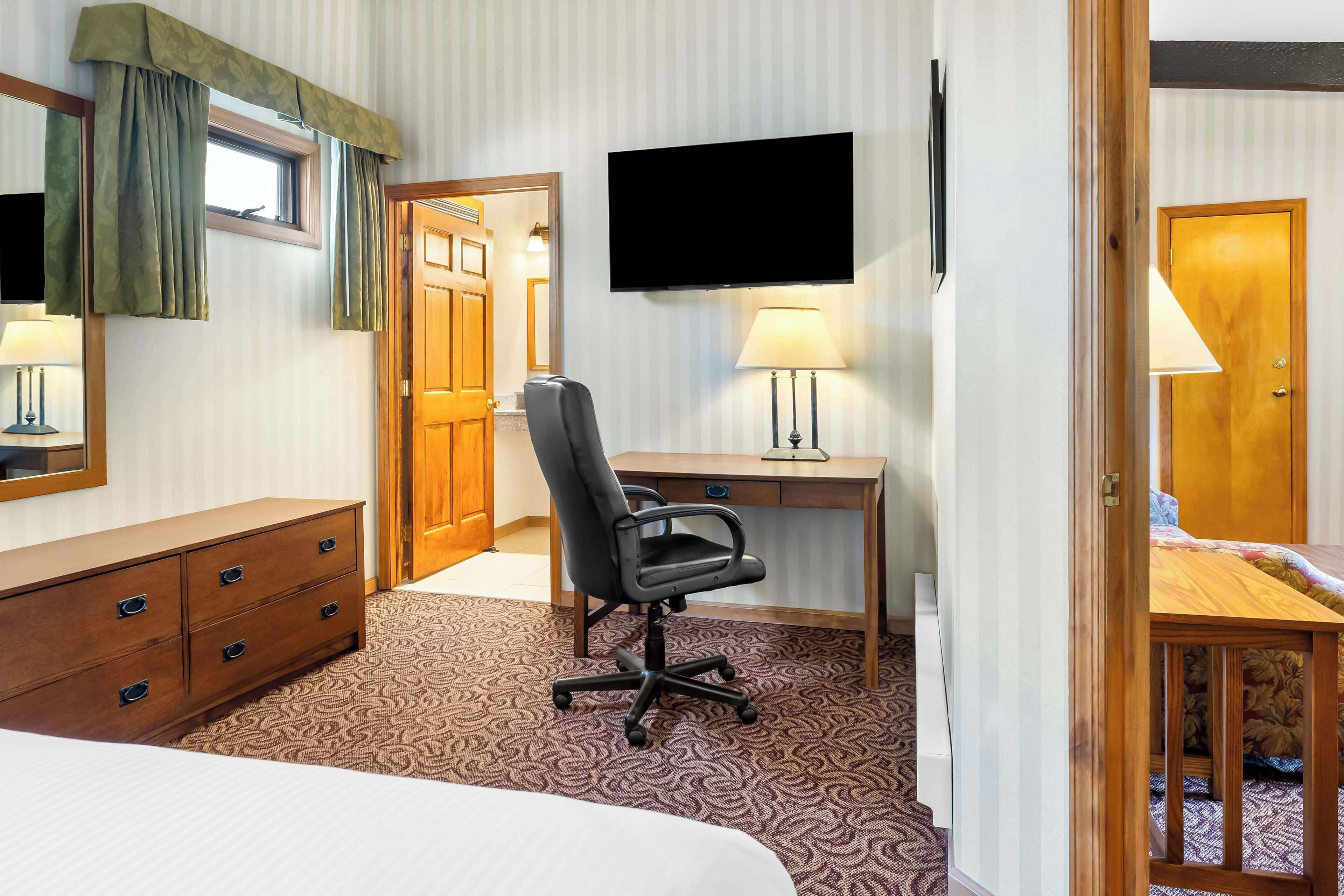 A hotel room with a bed, a desk with a chair, a TV, and a lamp.