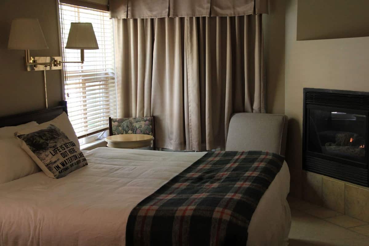 Una habitación de hotel con cama, una silla, una mesita, chimenea y cortinas.