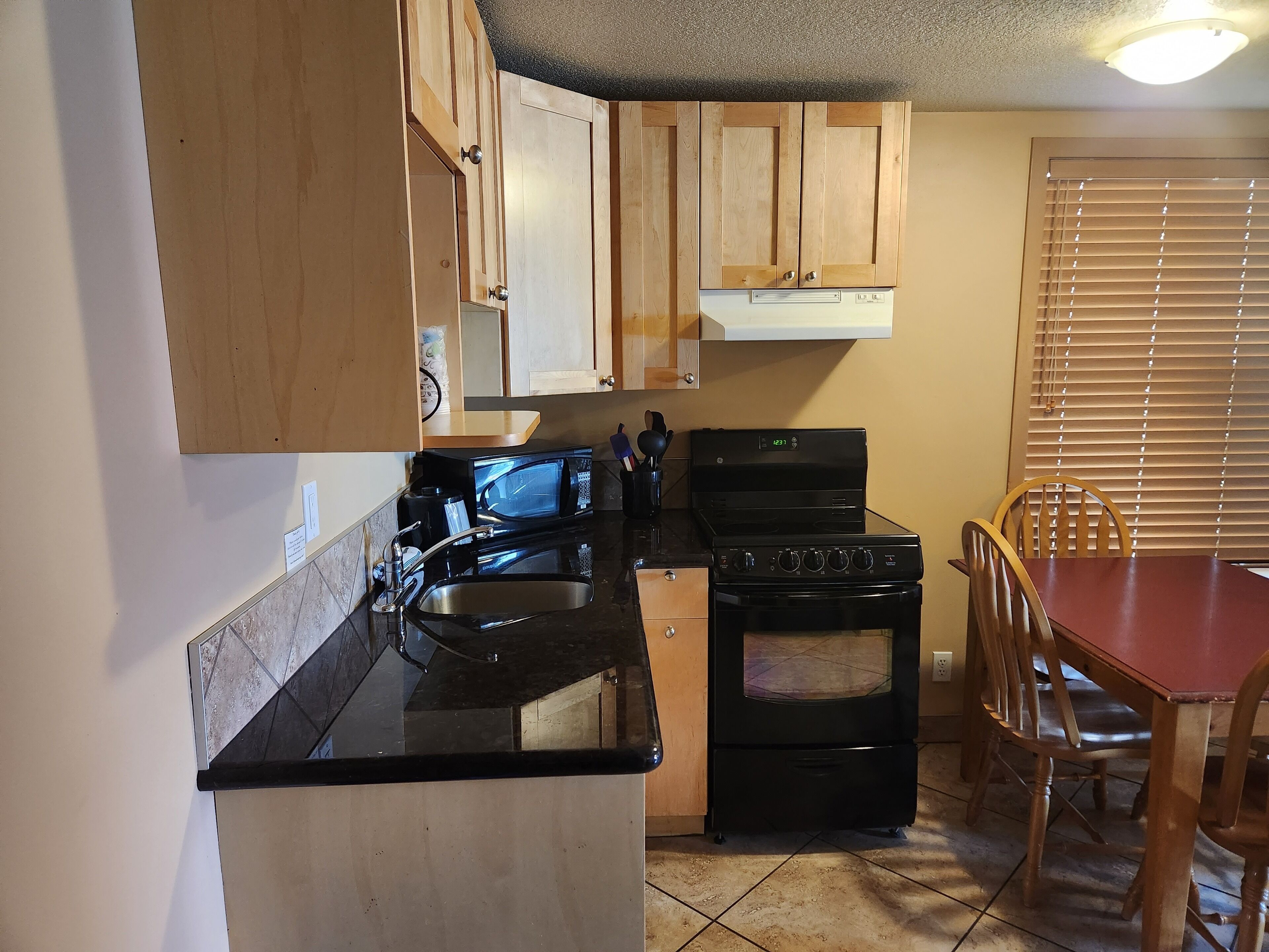 A compact kitchen with wooden cabinets, a black stove, a microwave, and a dining table with chairs.