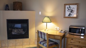 Une pièce avec une cheminée, une table avec une lampe, une chaise, un four à micro-ondes et une commode.