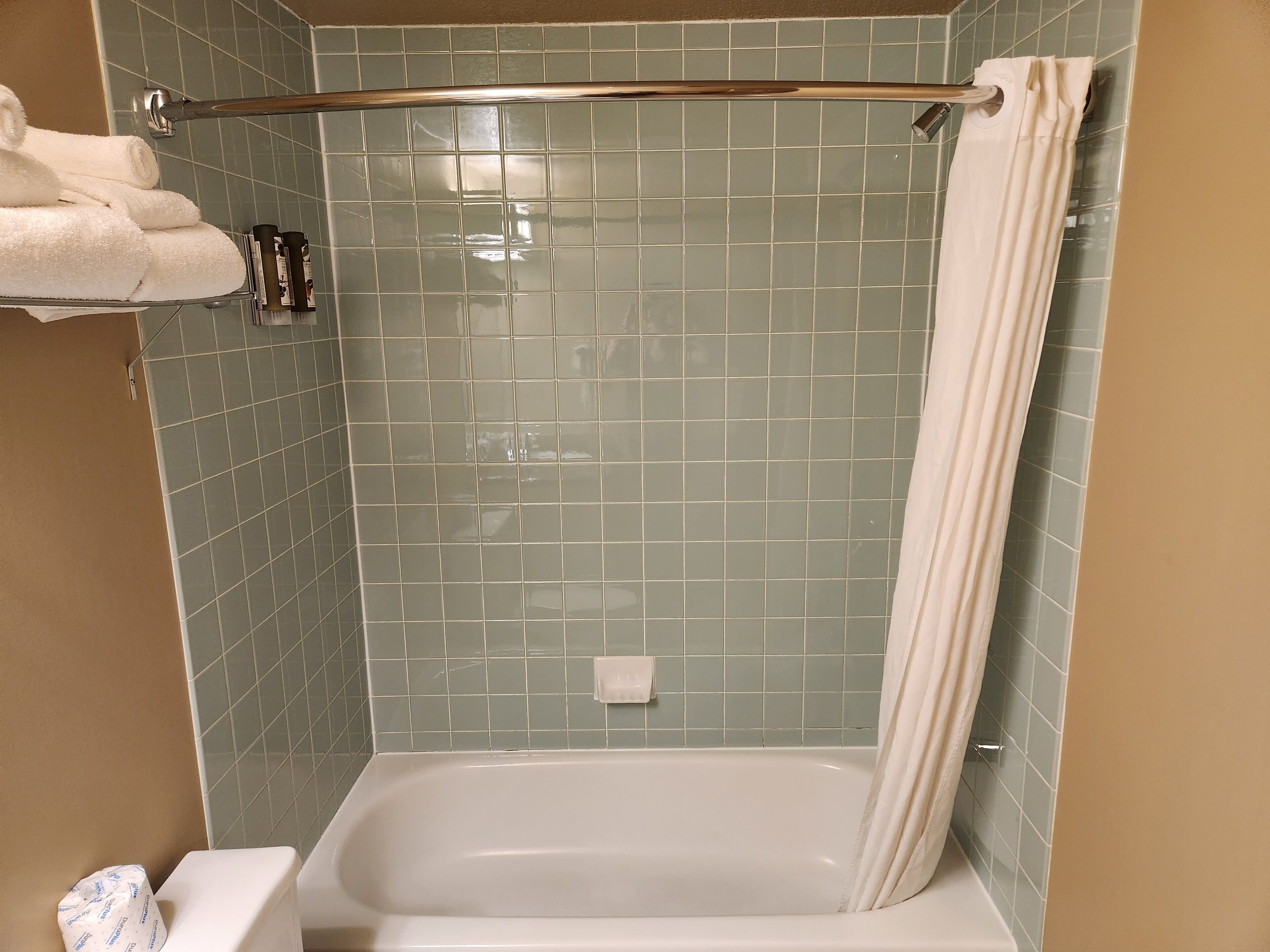 Een badkamer met een bad, douchegordijn en een handdoekrek met handdoeken.