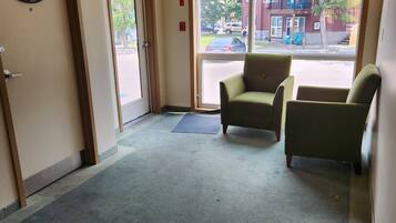 A hotel lobby with a green carpet, two armchairs, a door with a sign, and a view of the outside.