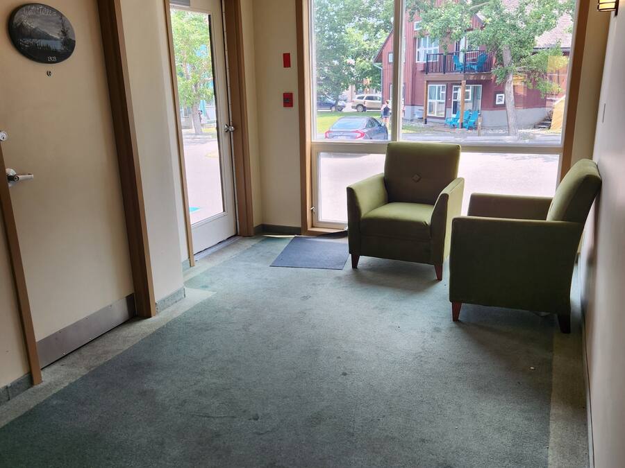 A hotel lobby with a green carpet, two armchairs, a door with a sign, and a view of the outside.