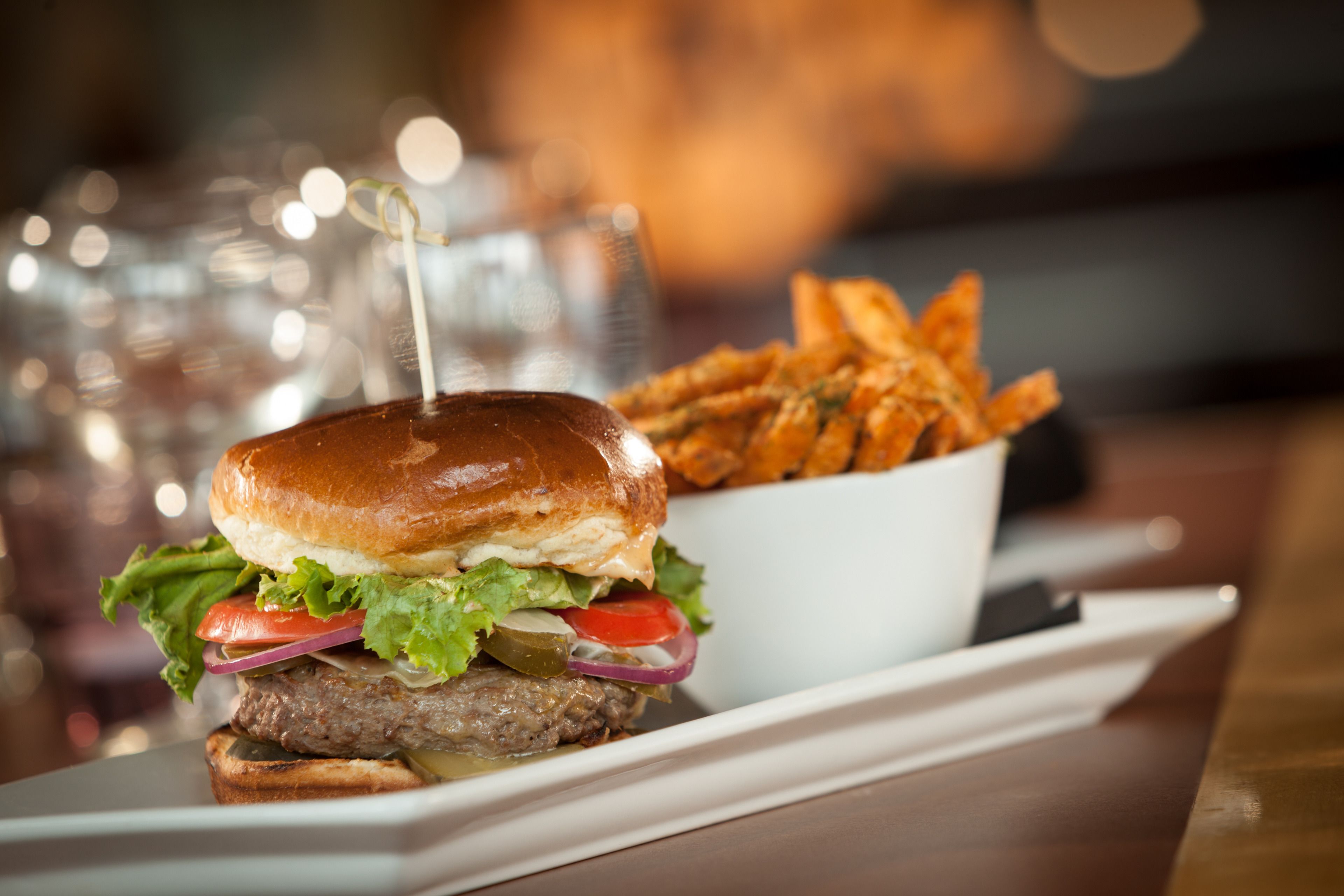 A burger with a bun, lettuce, tomato, and a pickled onion, served with a side of fries.