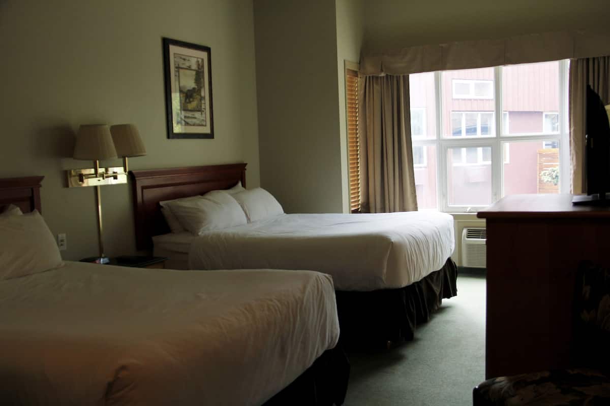 Habitación de hotel con dos camas, una lámpara de noche, un cuadro en la pared y una ventana con cortinas.