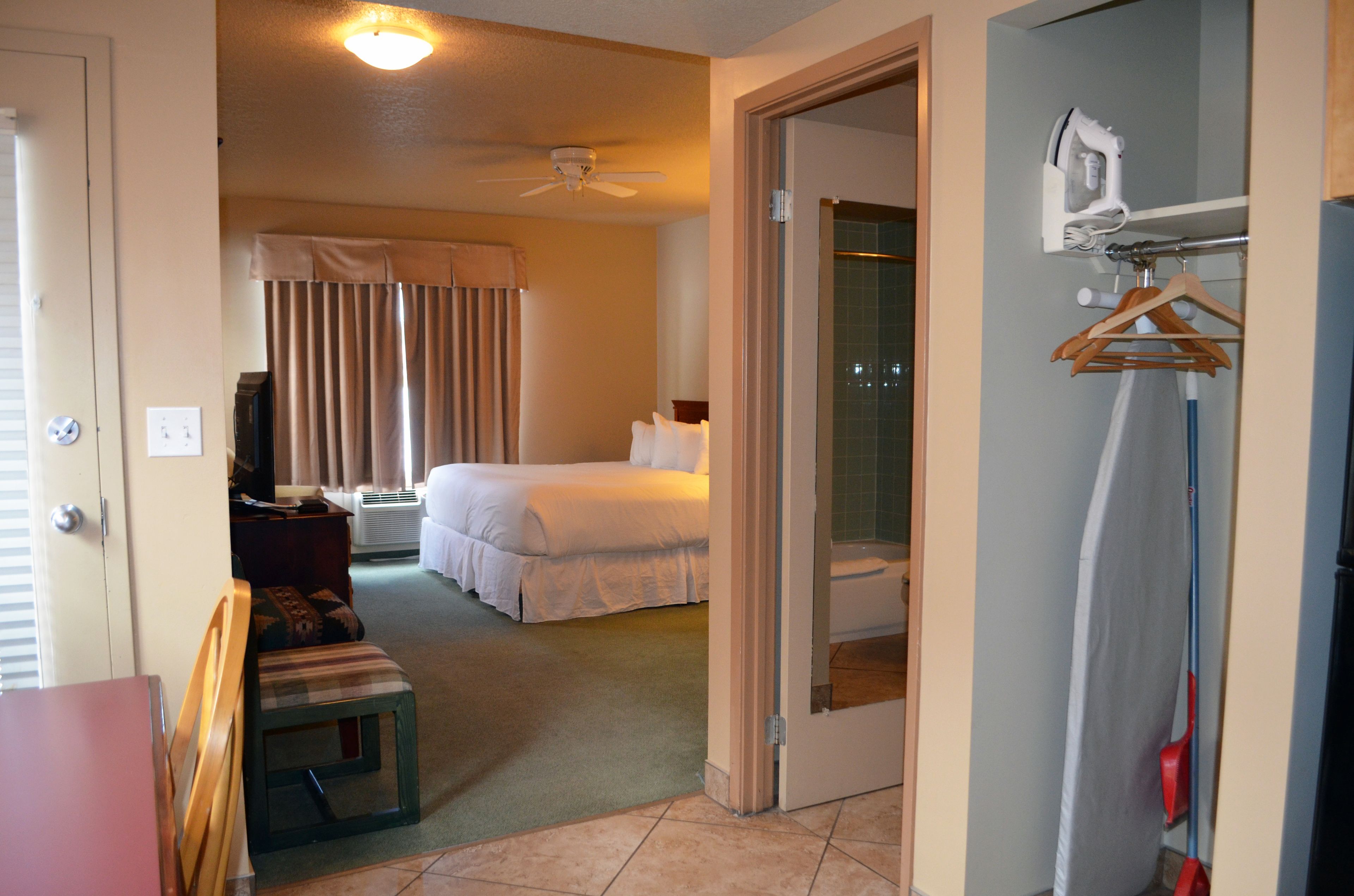 A hotel room with a bed, a desk with a chair, a ceiling fan, and a bathroom visible through an open door.