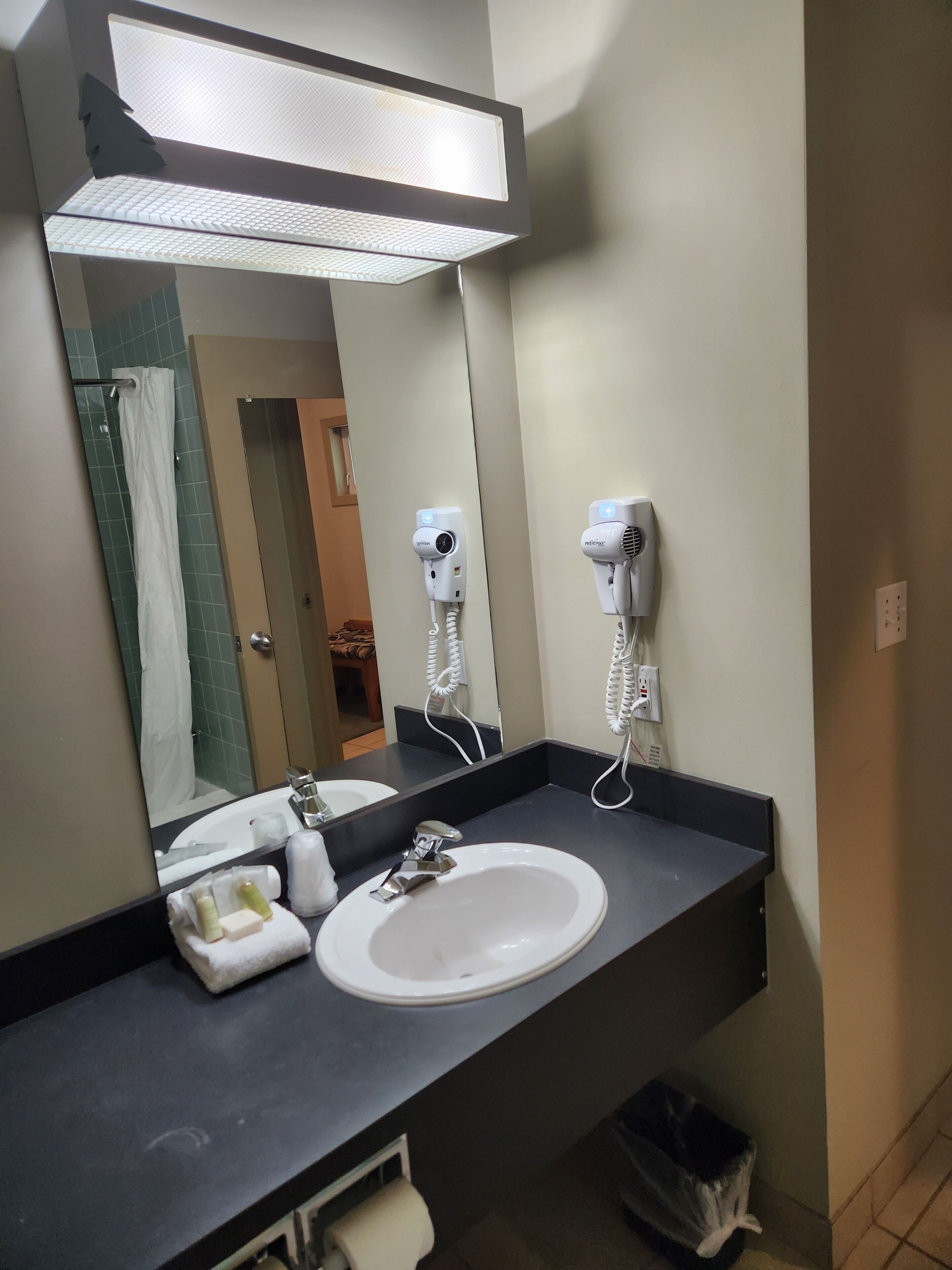 A bathroom with a white sink, a mirror, and two hair dryers mounted on the wall.
