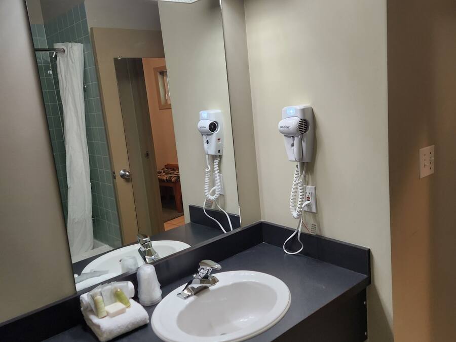 Un bany amb un lavabo blanc, un mirall i dos assecagats de pèl fixats a la paret.