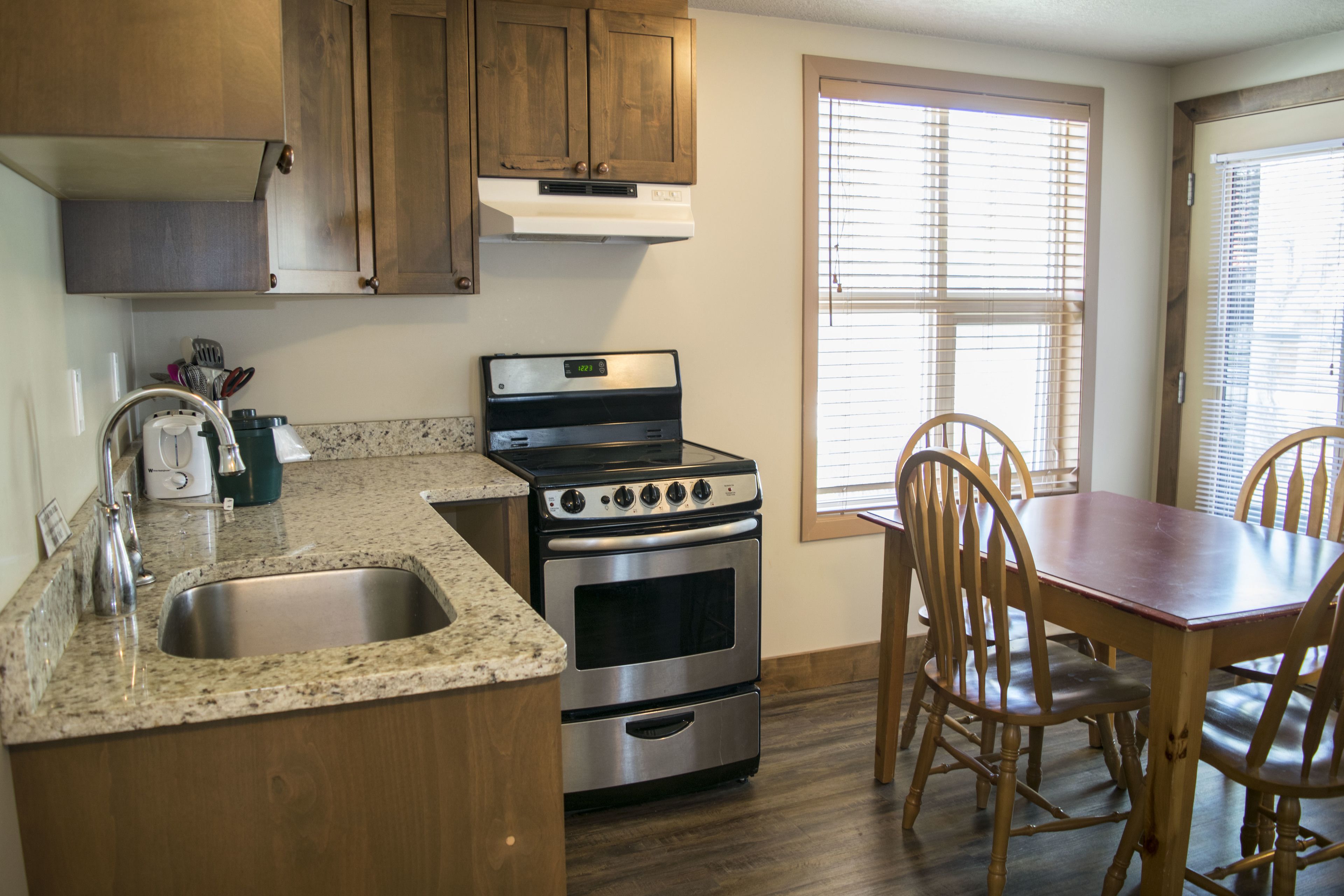 A kitchen with granite countertops, stainless steel appliances, wooden cabinets, and a dining area with a wooden table and chairs.